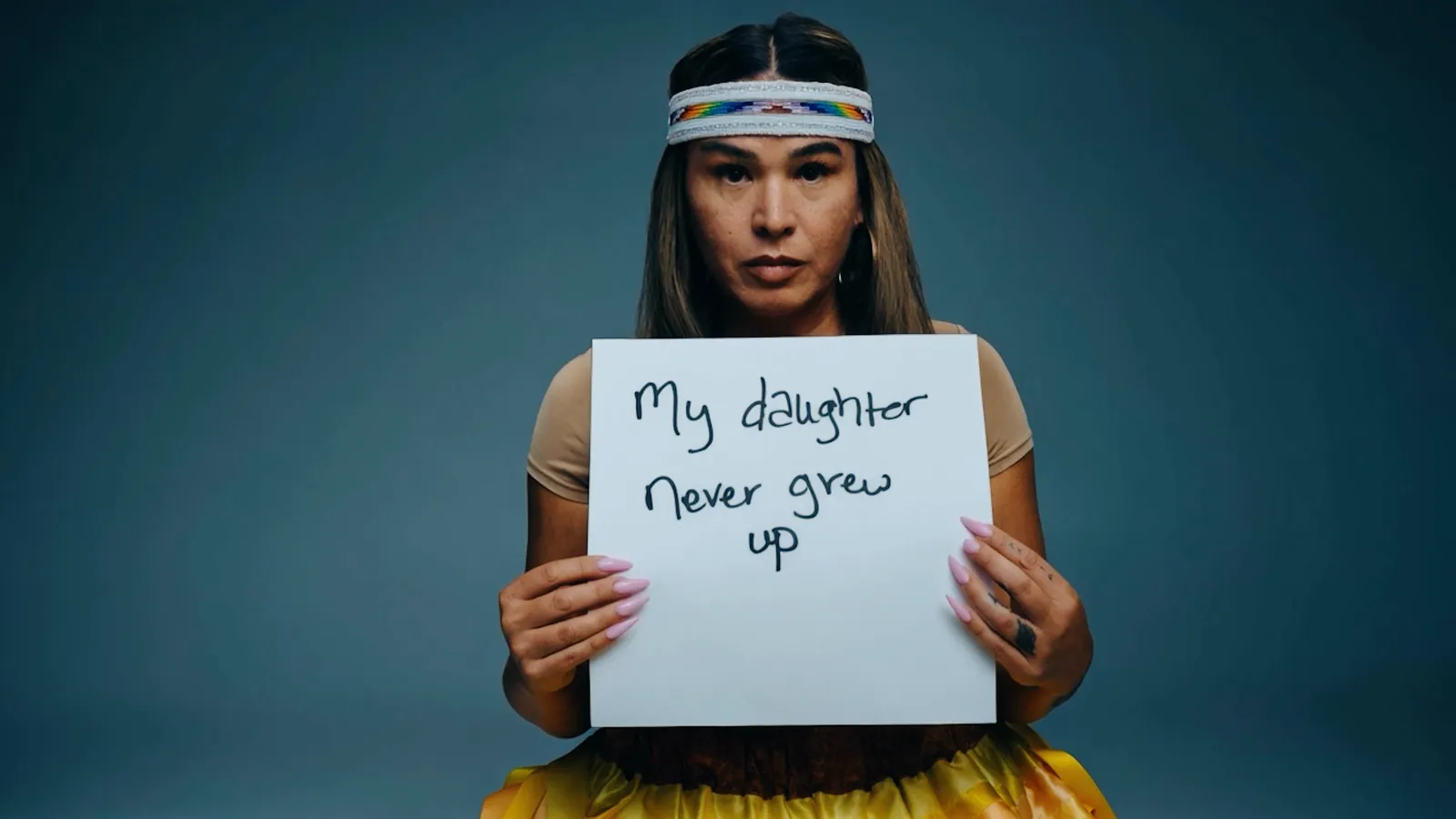 A woman holding a handwritten card that reads: my daughter never grew up
